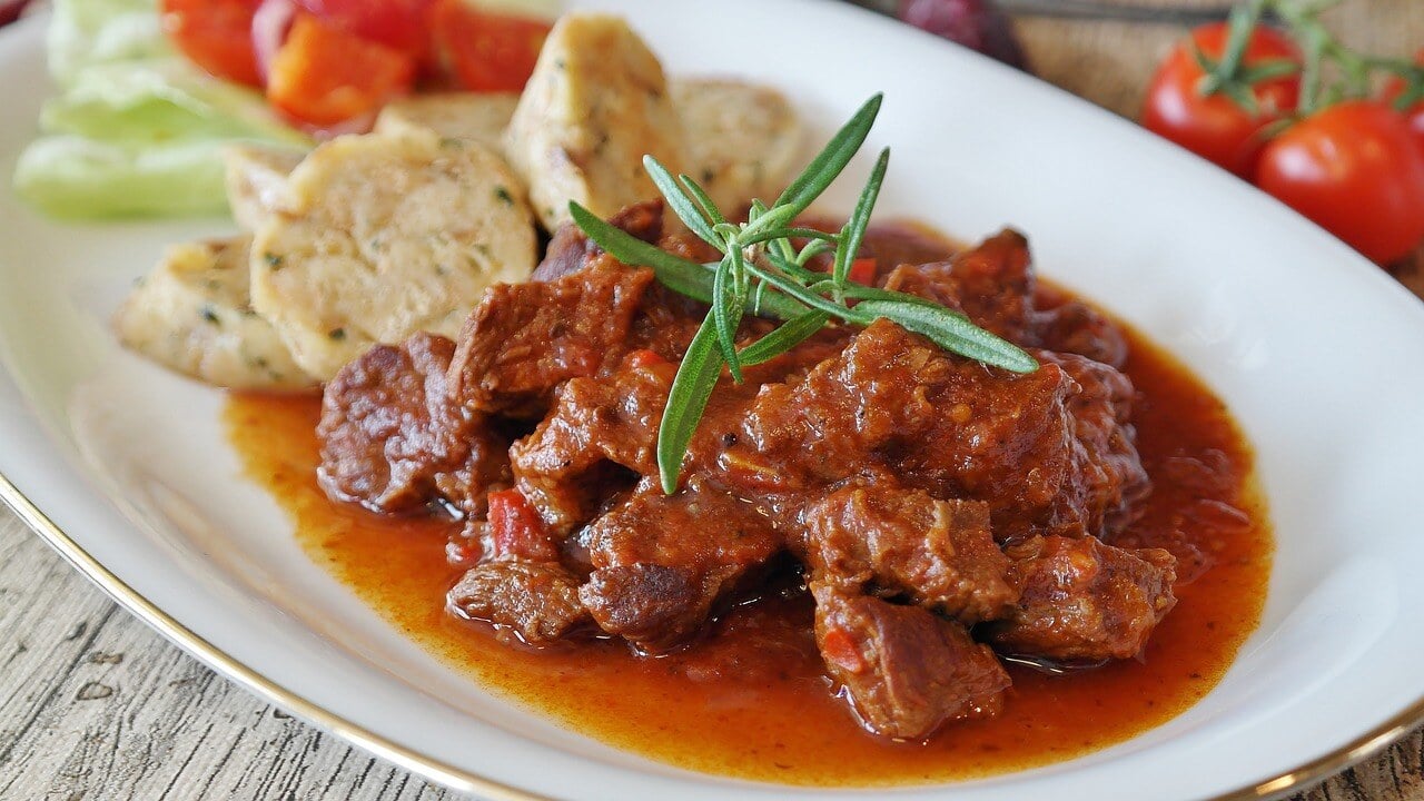 Goulash laden with paprika, alongside bread dumplings