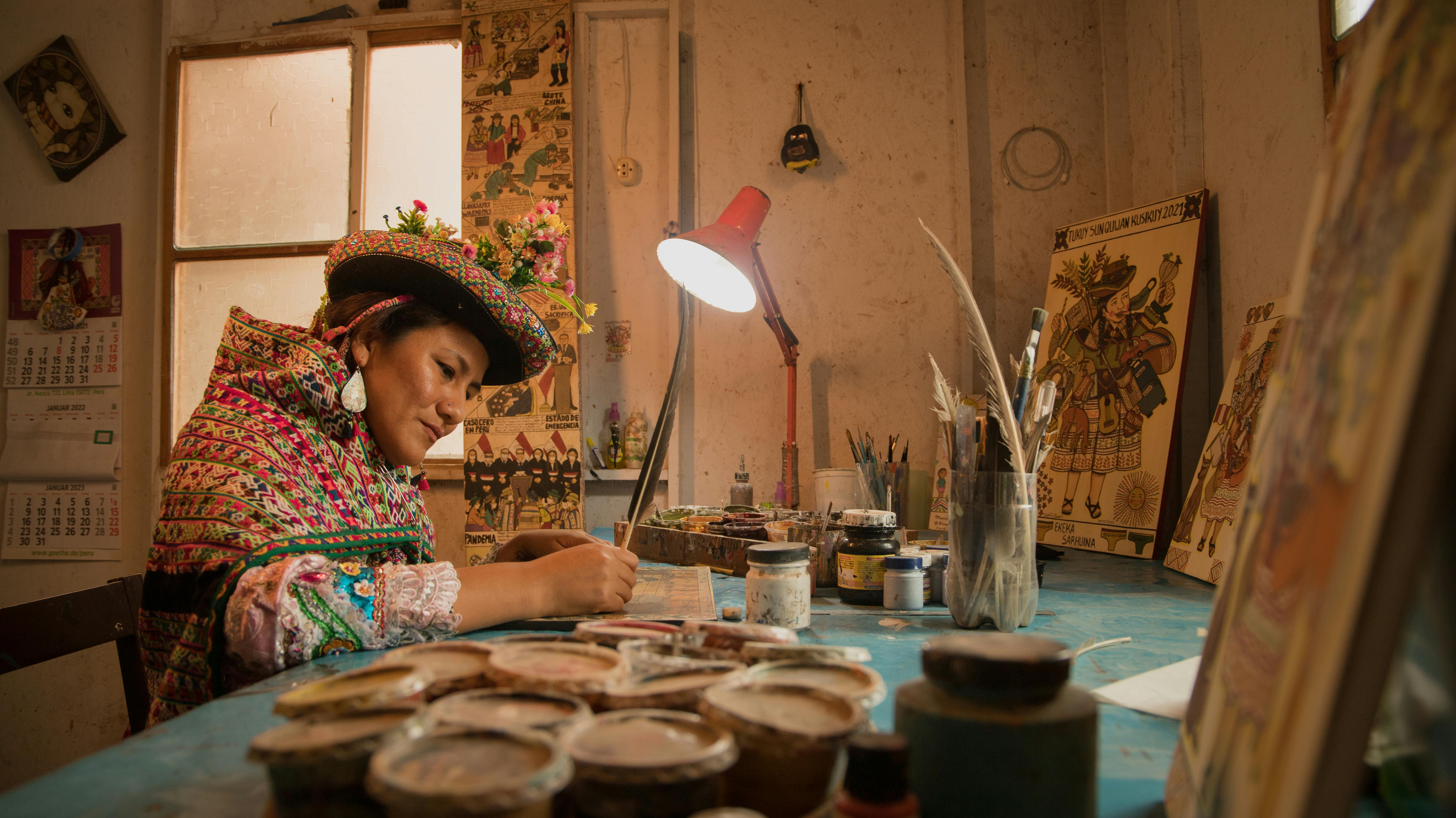 A woman wearing traditional clothing paints culturally significant images in a studio in Lima, Peru